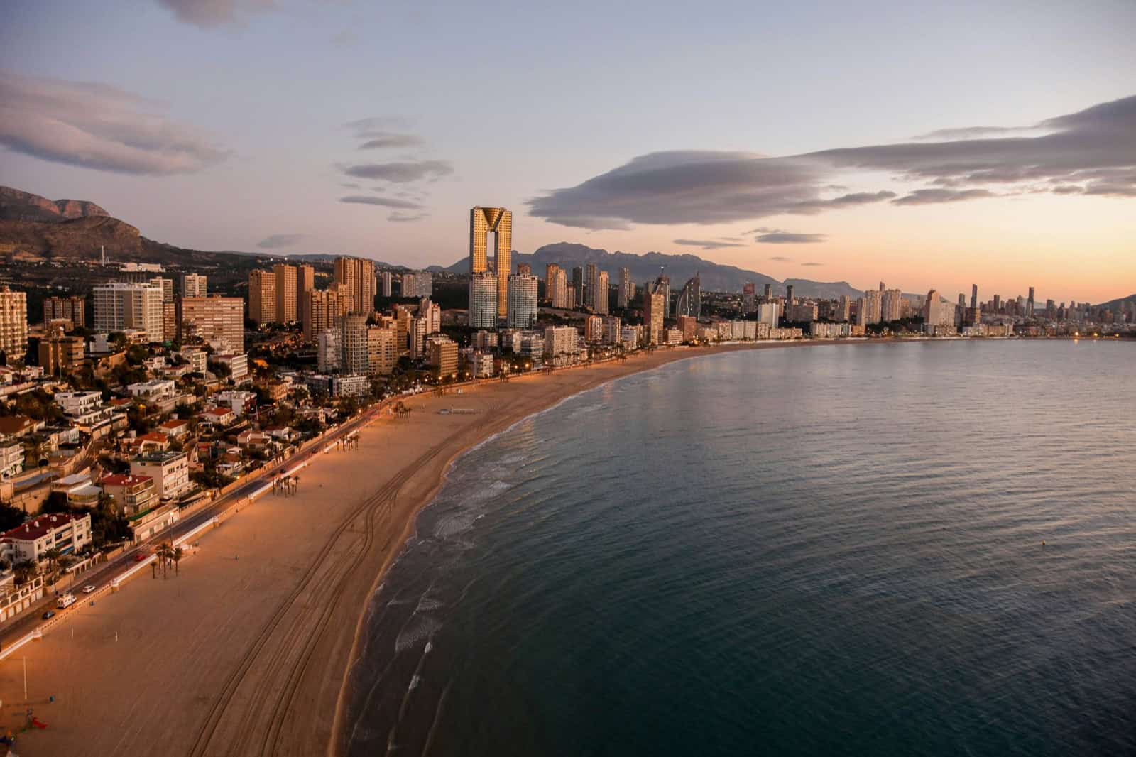 Vista aerea de Benidorm al atardecer, con el skyline residencial mediterraneo y la Torre Intempo destacando sobre la bahia.