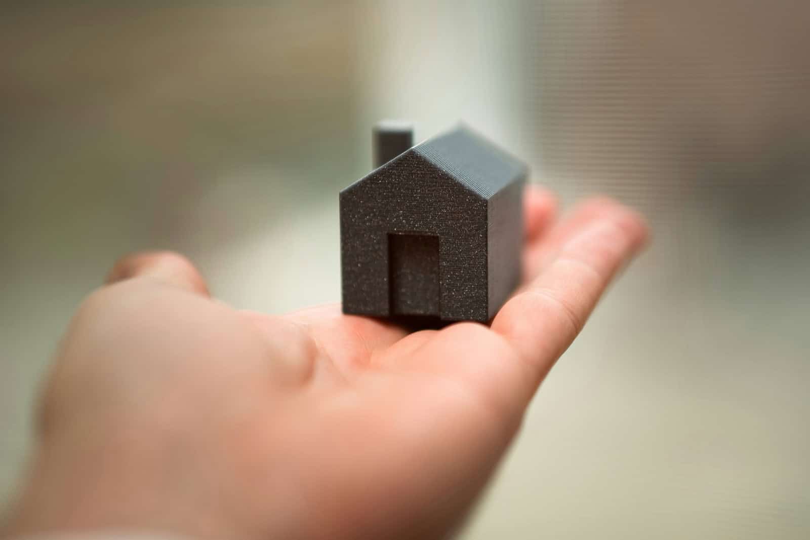Mano sosteniendo una pequena maqueta de casa, simbolo de la proteccion del hogar mediante seguros adaptados a comunidades de propietarios.